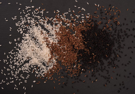 White, brown and black rice on black stone boardの写真素材