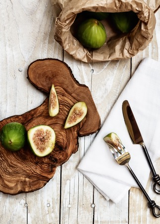 Cutted ripe green figs, fork and knife on rustic wooden tableの写真素材