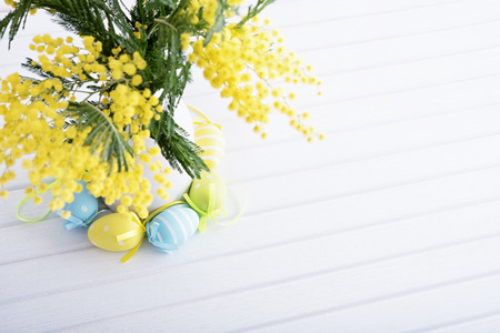 Vase of fresh mimosa with decorative easter eggs on wooden tableの写真素材