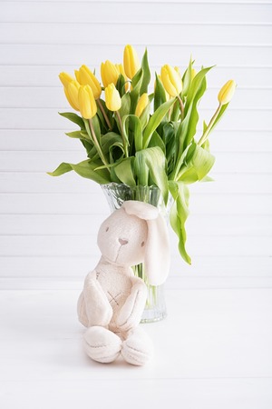 Yellow tulips in vase and white rabbit on wooden tableの写真素材