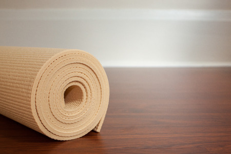Light yellow yoga mat rolled up on brown wood floor with space for copyの写真素材