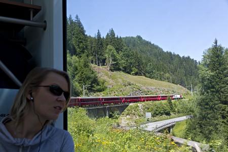 young pretty woman watches with amazement the alpine scenery pass by in the world famous swiss train Glacier Express, via earplugs she receives further information about train and sceneryの写真素材