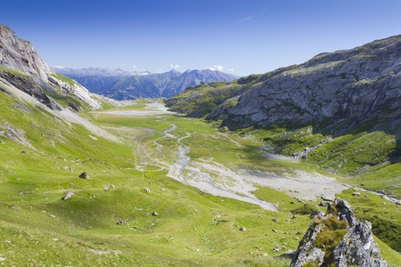 flat green high alpine valley crossed by little melt water streams running through and great mountain viewsの写真素材