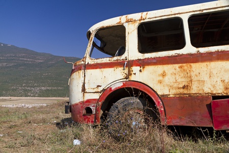 stripped rusty, old abandoned red bus wreck in arid mountainous landscape of Montenegroの写真素材