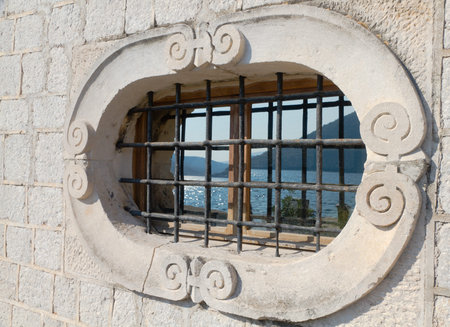 ornate carved  historic natural stone window with a mountainous bay reflecting in itの写真素材