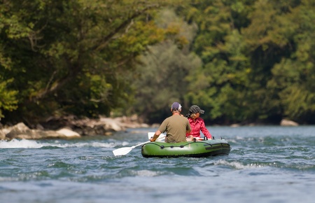 middle aged couple sits in rubber dinghy paddle in hand rowing together on a river in pretty natural summer settingsの写真素材