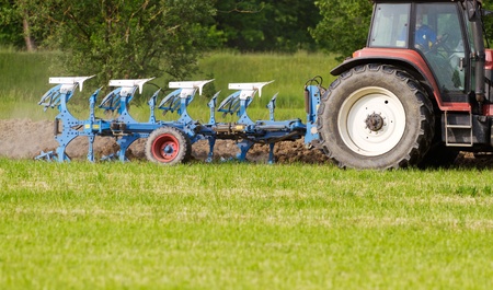 tractor with plough ploughing a grass covered field, concept for agriculture business のeditorial素材