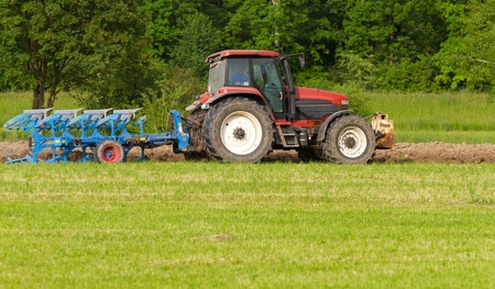 tractor with plough ploughing a grass covered field, concept for agriculture business の写真素材