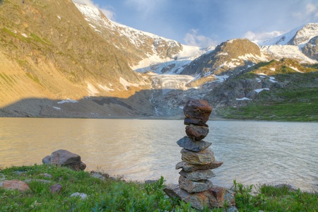 Swiss alpine mountain lake with rock cairn marking and a glacier near Susten pass in summer at sunset, Switzerlandの写真素材