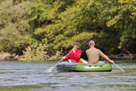 middle aged couple sits in rubber dinghy paddle in hand rowing together on a river in pretty natural summer settingsの写真素材