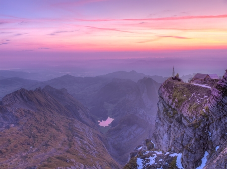 House on sheer rock cliff over high alpine ragged sharp karst mountain top ranges disapearing in misty distance at sunset, Switzerland の写真素材