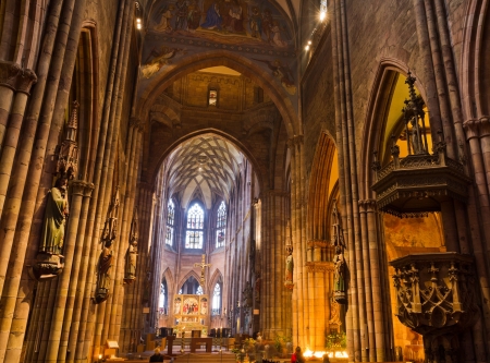 Interior with high ceilings, pillars, stained glass windows, wooden church benches, carved decoration figures of gothic, Freiburg minster Germany.のeditorial素材