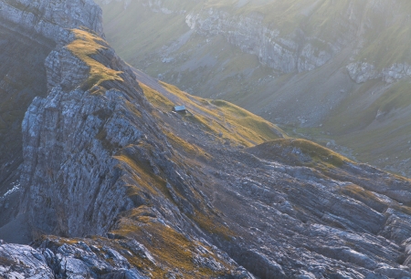 sheer rock twisted mountain ridge and single house in early morning mist at mount Saentis, Switzerlandの写真素材