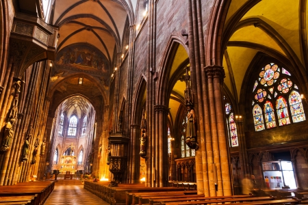 Interior with high ceilings, pillars, stained glass windows, wooden church benches, carved decoration figures of gothic, Freiburg minster Germany のeditorial素材