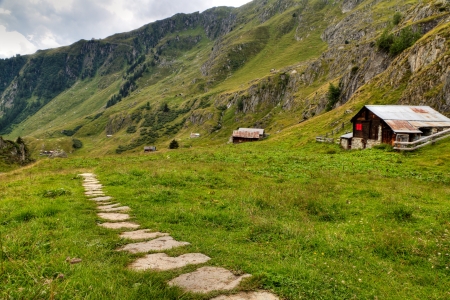 hiking path leading along alpine valley with wooden huts, Switzerlandの写真素材