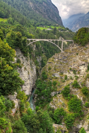 arch train bridge crossing deep cut river valley at Stalden Saas, valais, Switzerlandの写真素材