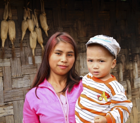 HPA AN, BURMA-OCT.  30: Young unidentified village woman stands in front of her hut wall from woven bamboo with corn knobs drying holding her child on October 30, 2011 in Hpa An, Burma.  のeditorial素材