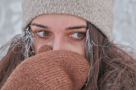A young attractive woman hides her face from the cold.