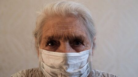Close-up senior woman puts on a protective medical mask.の写真素材