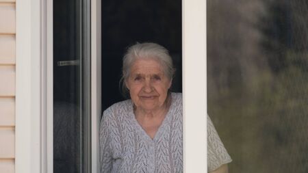 The old woman looks out of the window and smiles.の写真素材