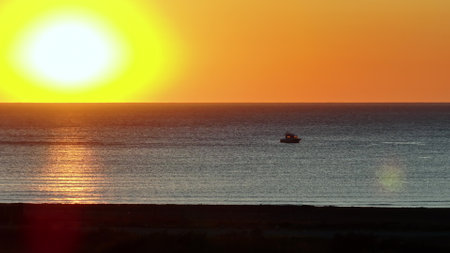 Sun Setting Over Ocean With Boat in Waterの写真素材