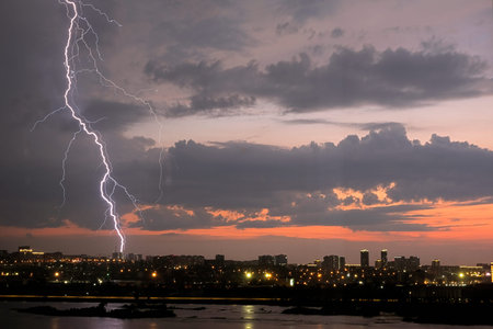Lightning strikes over a city skyline during a dramatic sunset with stormy clouds looming