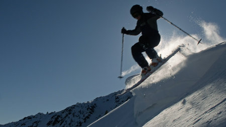 Professional skier jumping from snowy mountain ridge in bright sunlightの写真素材