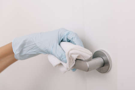 Cleaning black door handles with an antiseptic wet wipe in blue gloves. Sanitize surfaces prevention in hospital and public spaces against corona virus. Woman hand using towel for cleaningの写真素材
