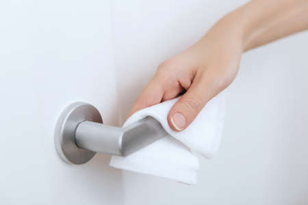 Cleaning door handles with an antiseptic wet wipe and gloves. Sanitize surfaces prevention in hospital and public spaces against corona virus. Woman hand using towel for cleaning home room door linkの写真素材