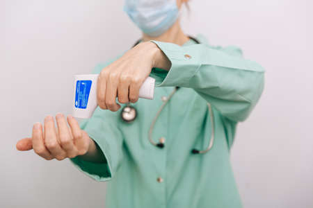 Temperature measurement gun in doctor hands. Close-up shot of doctor wearing protective surgical mask ready to use infrared isometric thermometer gun to check body temperature for virus symptomsの写真素材