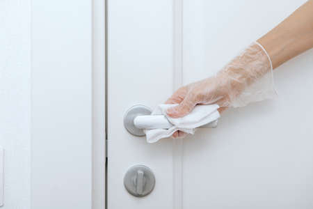 Cleaning door handles with wet wipe and white gloves. Woman hand using towel for cleaning home room door link. Sanitize surfaces prevention in hospital and public spaces against corona virusの写真素材