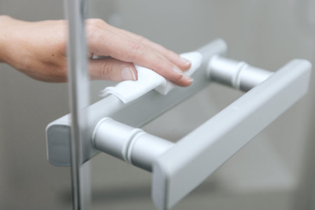 Cleaning glass door handles with an antiseptic wet wipe. Woman hand using towel for cleaning home room door link. Sanitize surfaces prevention in hospital and public spaces against corona virusの写真素材