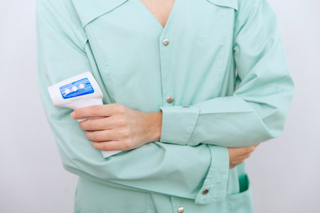 Temperature measurement gun in doctor hands. Close-up shot of doctor wearing protective surgical mask ready to use infrared isometric thermometer gun to check body temperature for virus symptomsの写真素材