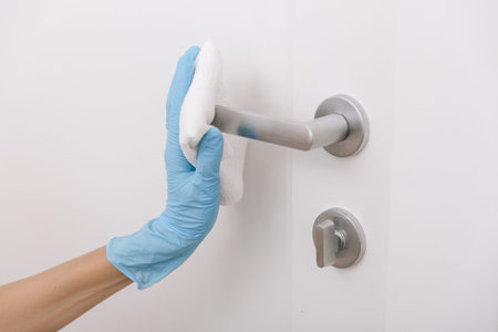 Cleaning black door handle with an antiseptic wet wipe in blue gloves. Woman hand using towel for cleaning. Sanitize surfaces prevention in hospital and public spaces against corona virusの写真素材