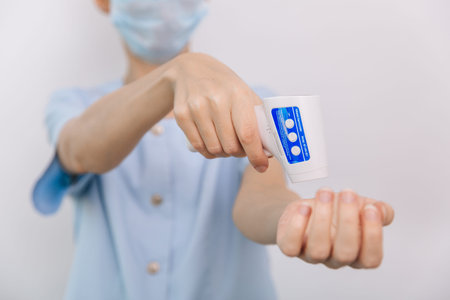 Temperature measurement gun in doctor hands. Close-up shot of doctor wearing protective surgical...
