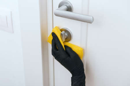 Cleaning door handle with yellow wipe in black gloves. Woman hand using towel for cleaning. Disinfection in hospital and public spaces against virusの写真素材