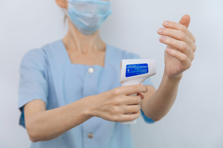 Temperature measurement gun in doctor hands. Close-up shot of doctor wearing protective surgical...