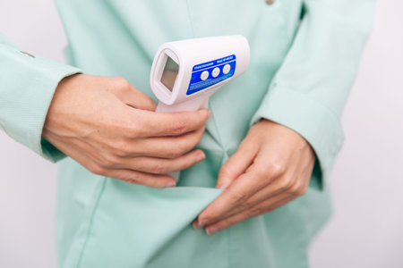 Temperature measurement gun in doctor hands. Close-up shot of doctor wearing protective surgical...