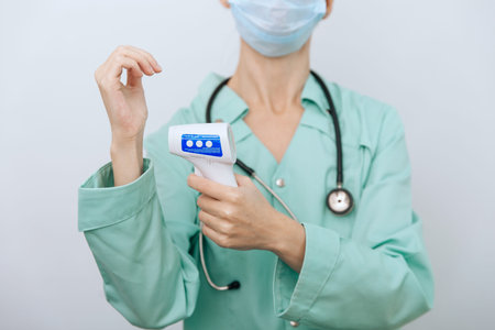 Temperature measurement gun in doctor hands. Close-up shot of doctor wearing protective surgical...
