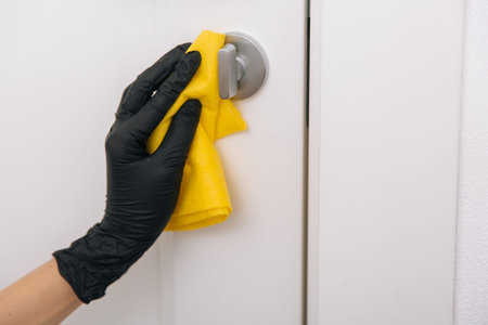 Cleaning door handle with yellow wipe in black gloves. Woman hand using towel for cleaning....