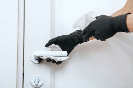 Cleaning door handle with dirty wipe in black gloves and sanitizer spray. Disinfection in hospital and public spaces against corona virus. Woman hand using towel for cleaningの写真素材