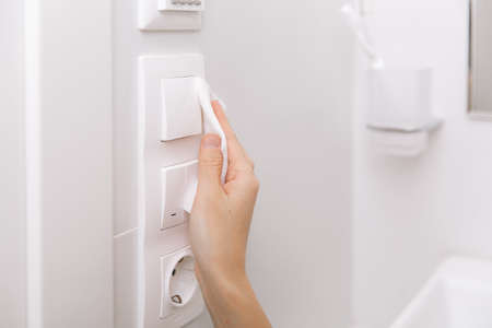Cleaning switches and sockets with a microfiber cloth. Sanitize surfaces prevention in hospital and public spaces against virus. Woman hand using wet wipe for cleaning home room door linkの写真素材