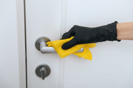 Cleaning door handle with yellow wipe in black gloves. Woman hand using towel for cleaning.
