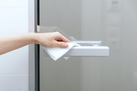 Cleaning glass door handles with an antiseptic wet wipe. Woman hand using towel for cleaning home...