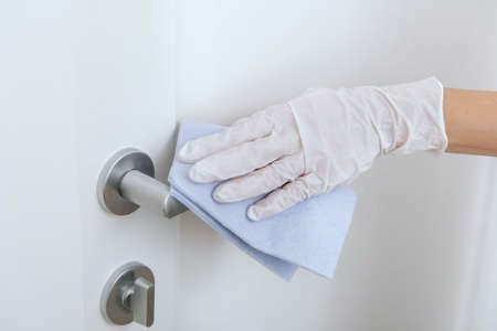Cleaning door handle with blue wipe in white gloves. Woman hand using towel for cleaning home room door link. Sanitize surfaces prevention in hospital and public spaces against corona virus.の写真素材