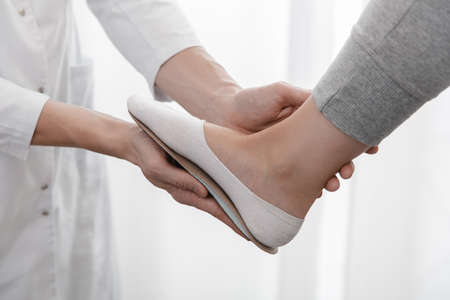 Doctor hands hold an orthopedic insole. Orthopedist tests the medical device. Orthopedic insoles on a white background. Foot care, comfort for the feet. Prevention of flat feet and foot diseases.の写真素材