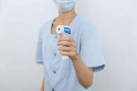 Temperature measurement gun in doctor hands. Close-up shot of doctor wearing protective surgical...