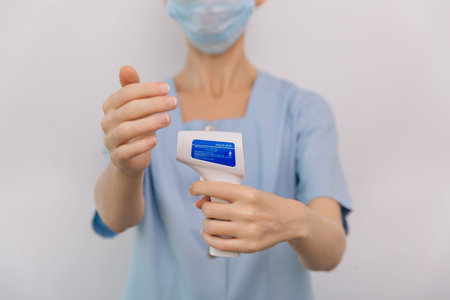 Temperature measurement gun in doctor hands. Close-up shot of doctor wearing protective surgical...