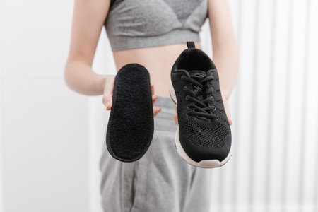 Fitness woman in sportswear with orthopedic insoles and sneakers. Woman putting orthopedic insole into shoe at home close up. Foot care banner. Flat Feet Correctionの写真素材
