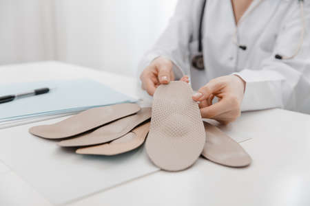 Doctor holding an insole while sitting at a table. Orthopedist tests the medical device. Orthopedic insoles. Foot care. Flat Feet Correction. Treatment and prevention of flat feet and foot diseasesの写真素材